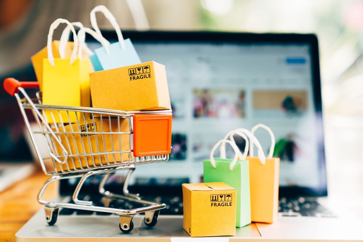 Boxes and shopping bags in a miniature shopping cart on top of a laptop