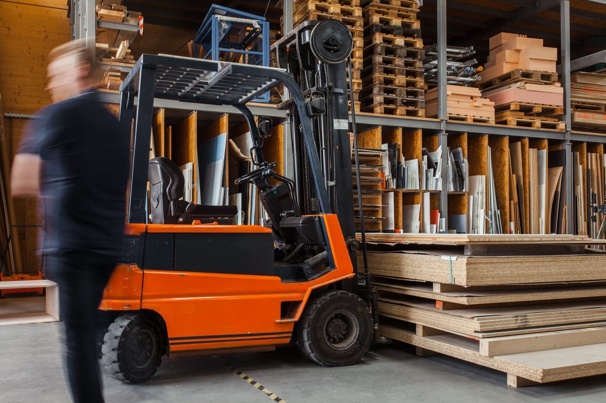 A forklifter moving a pile of wooden planks.