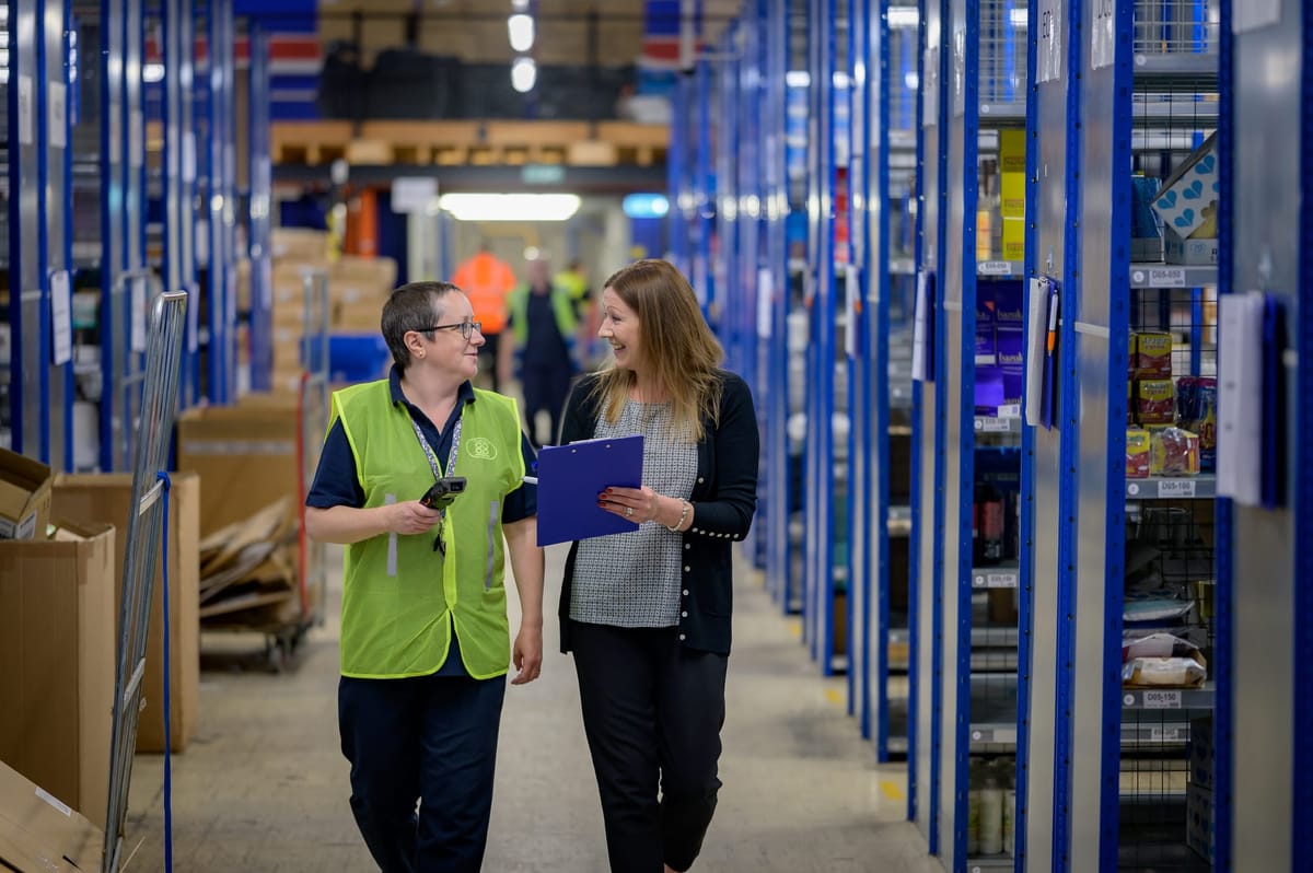 Two people walking down the hallway of a warehouse.