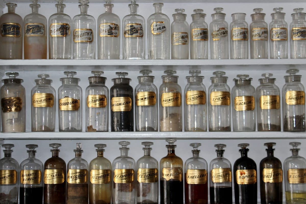 Rows of vintage glass bottles with gold labels on shelves, likely in an apothecary or museum setting.