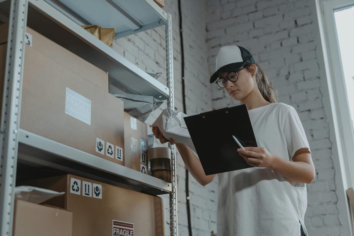 Alt text: A person holding a black clipboard in one hand and a white pack in the other, standing beside a shelf.