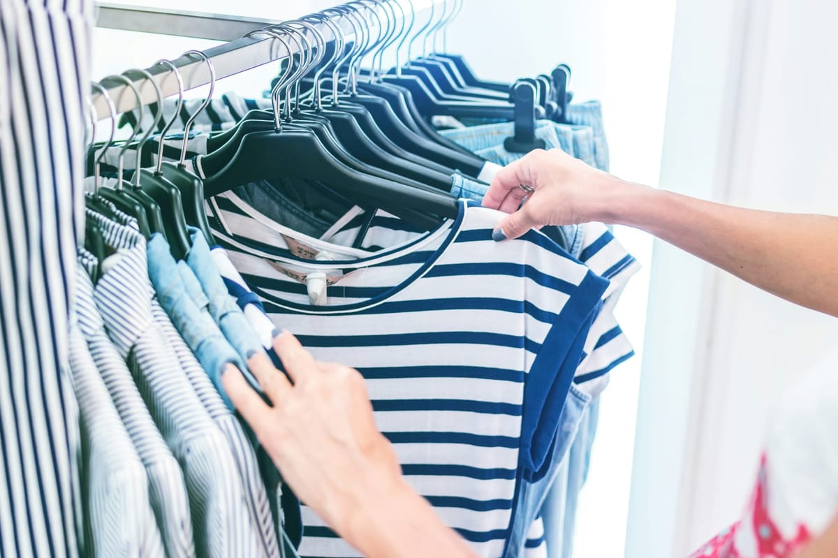 A shopper browses striped shirts on a clothing rack, inspecting fabric and style in a retail environment.