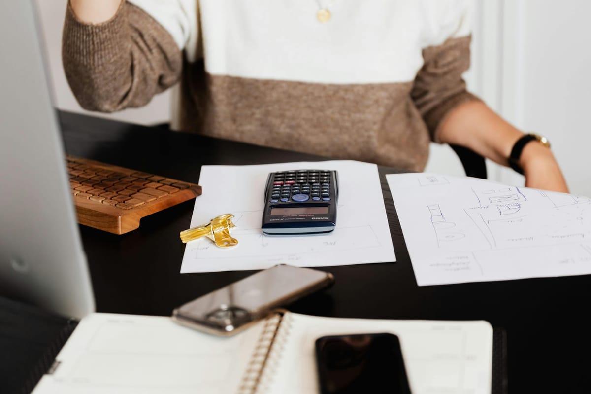 Person working at desk with calculator, house keys, floor plan sketches, and smartphone.