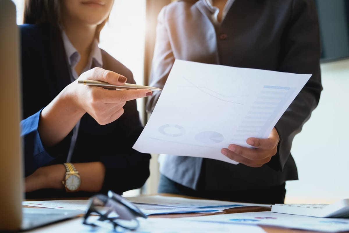 An auditor holds a pen pointing to documents for examination.