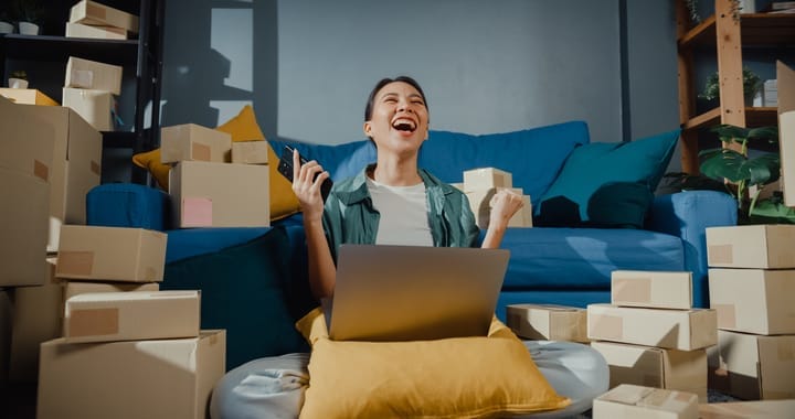 Young Asian female seller worker online store using mobile phone preparing parcel for shipment to client at home.