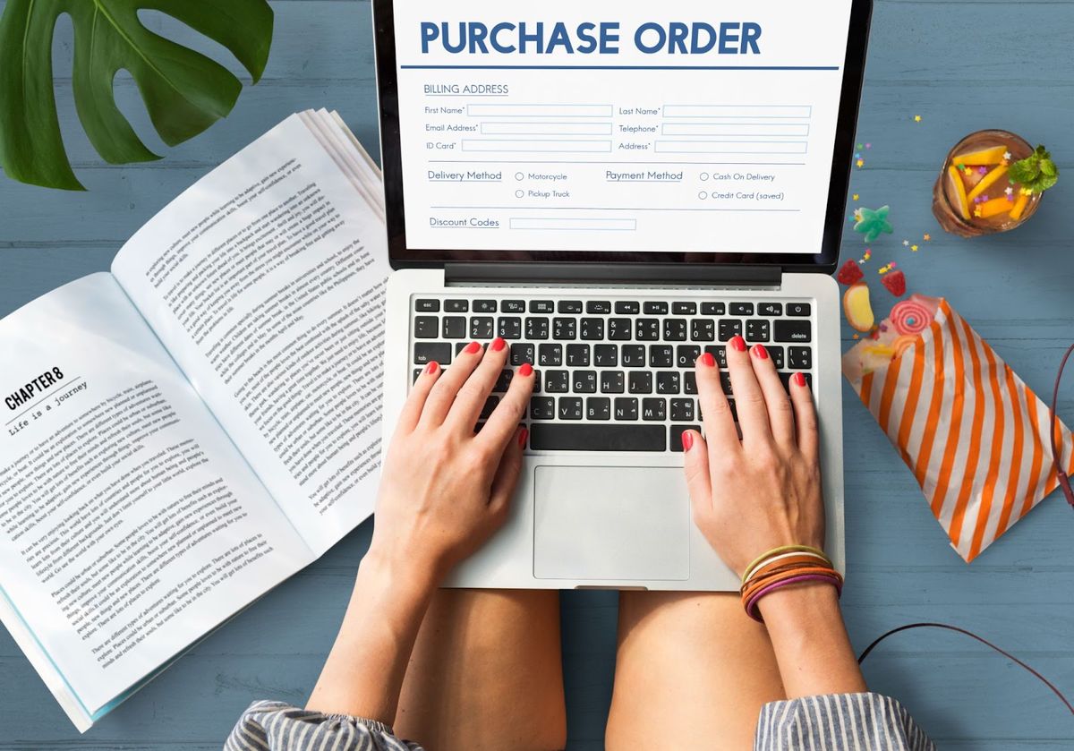 A person typing on a laptop displaying a purchase order form with billing address, delivery method, and payment options fields.