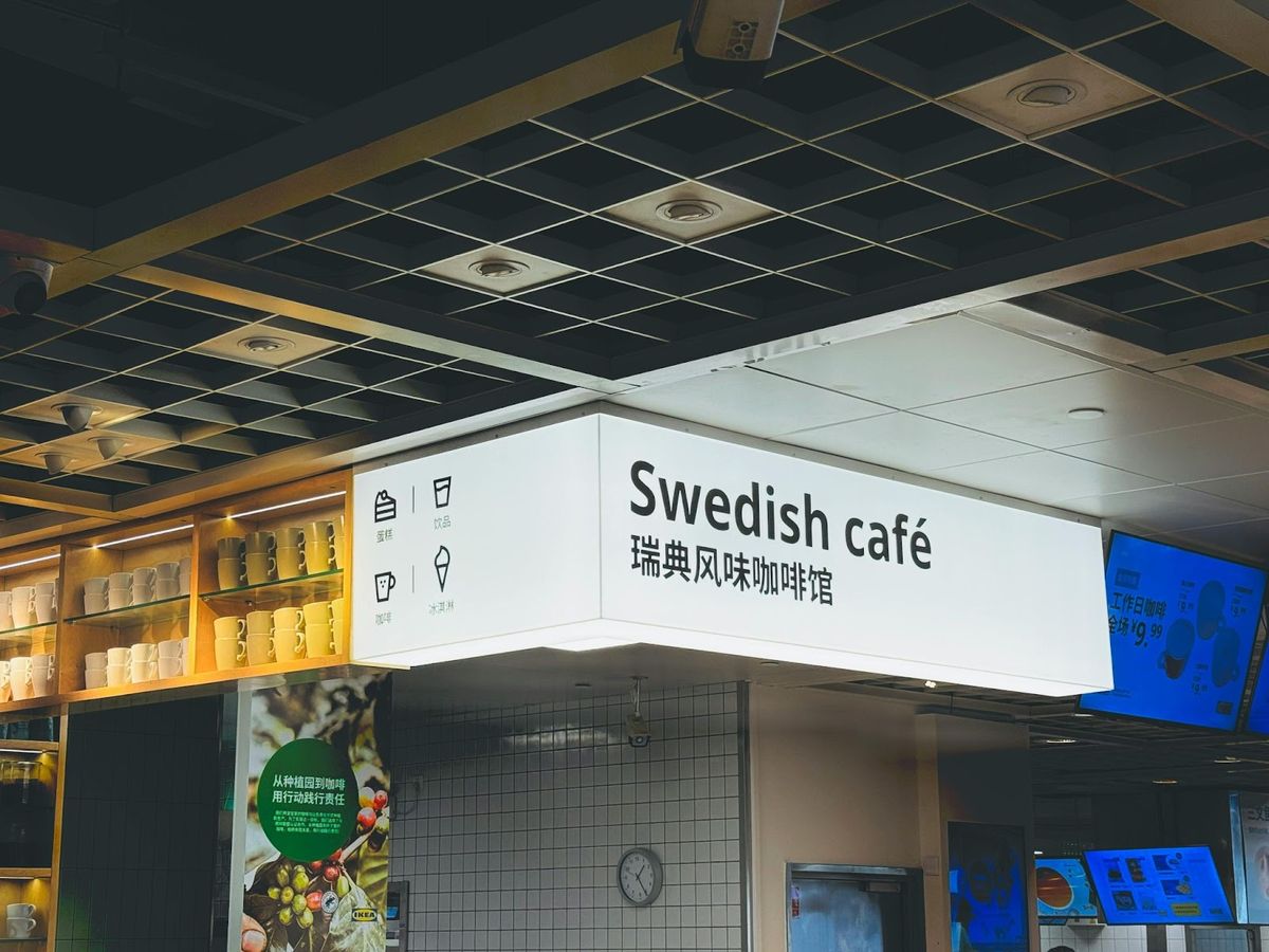 Lit sign for a Swedish café with cups displayed on nearby shelves.