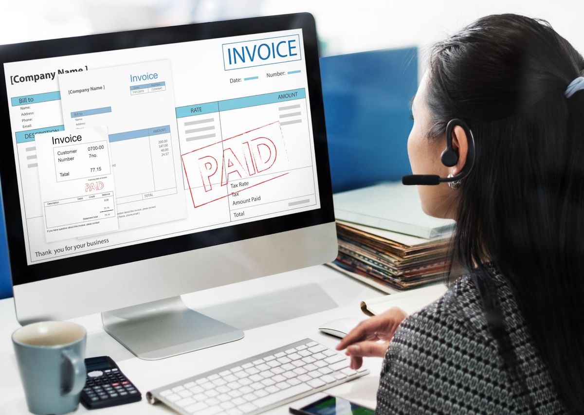 A person wearing a headset working at a computer displaying invoice templates with billing details on the screen.