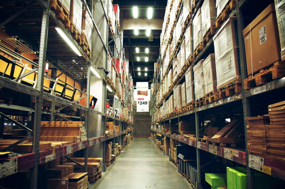 Warehouse aisle with tall racks of flat-pack boxes under bright lights.