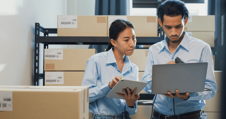 Empleados revisando información en un portátil y una tablet en un almacén, gestionando inventario en tiempo real.