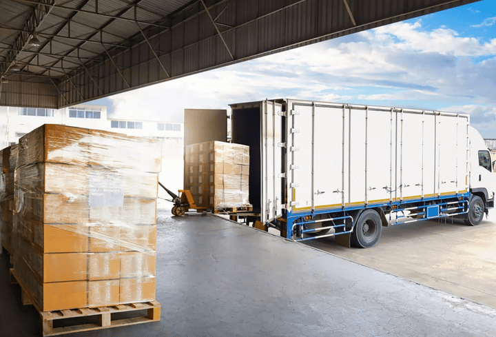 Camiones contenedores estacionados cargando palets de cajas en el muelle del almacén