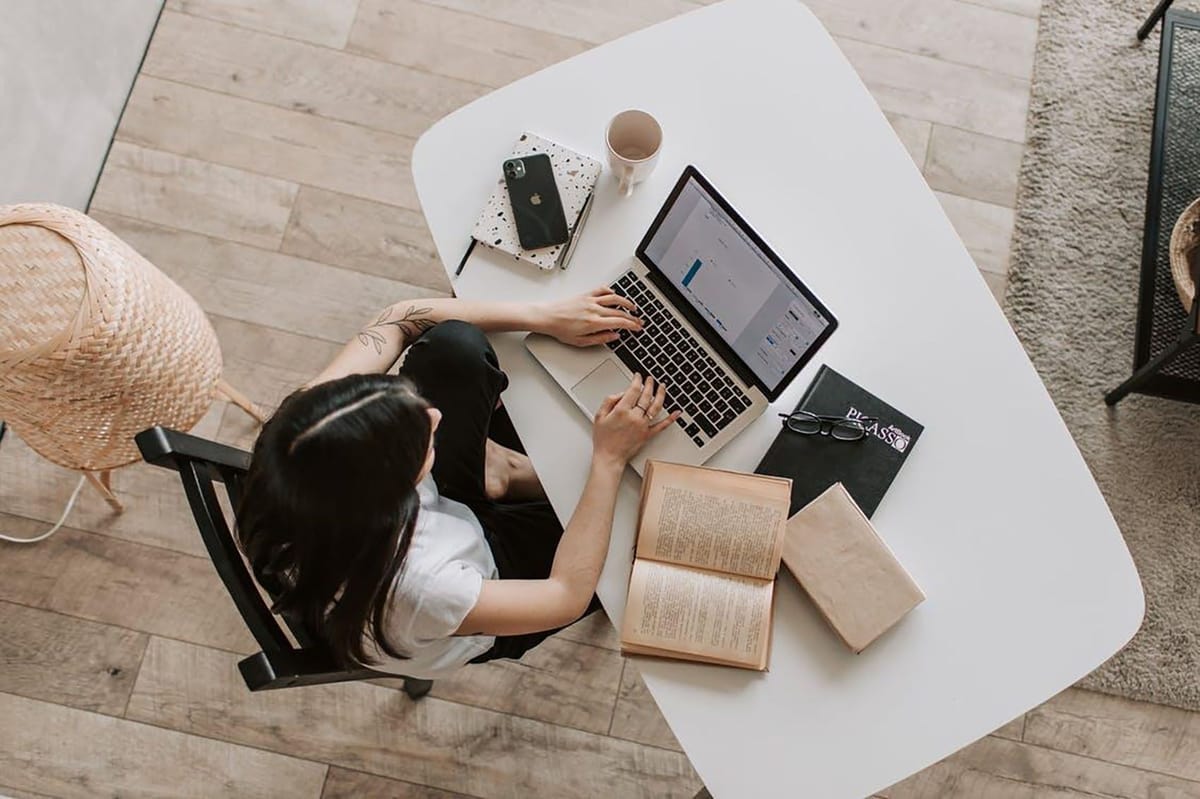 Overhead view of person working on laptop at home desk with books, coffee, and smartphone.