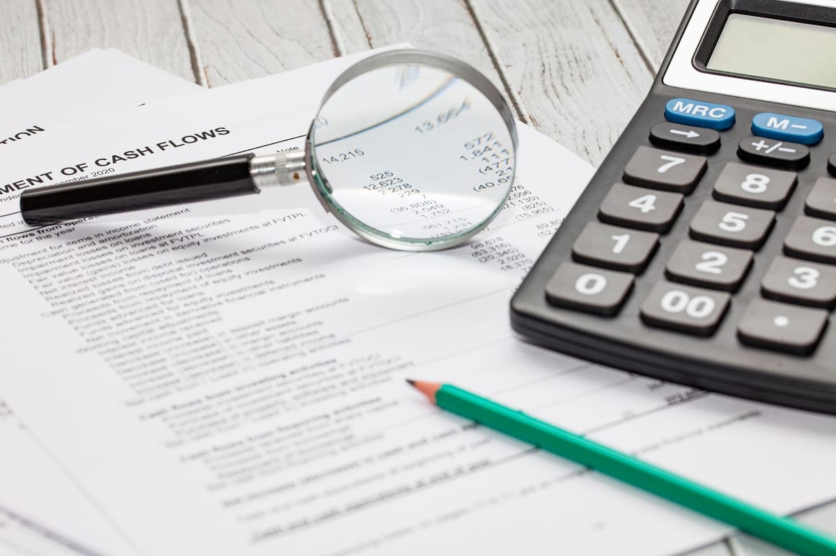 A Cashflow Statement, a magnifying glass, a penceil, and a calculator laying on a wooden desk
