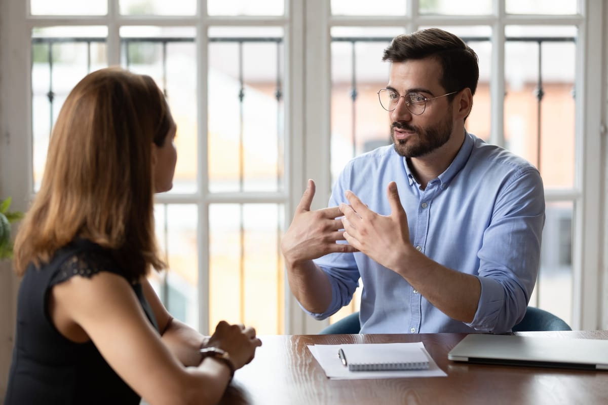 A man in glasses explaining to a woman in the office.