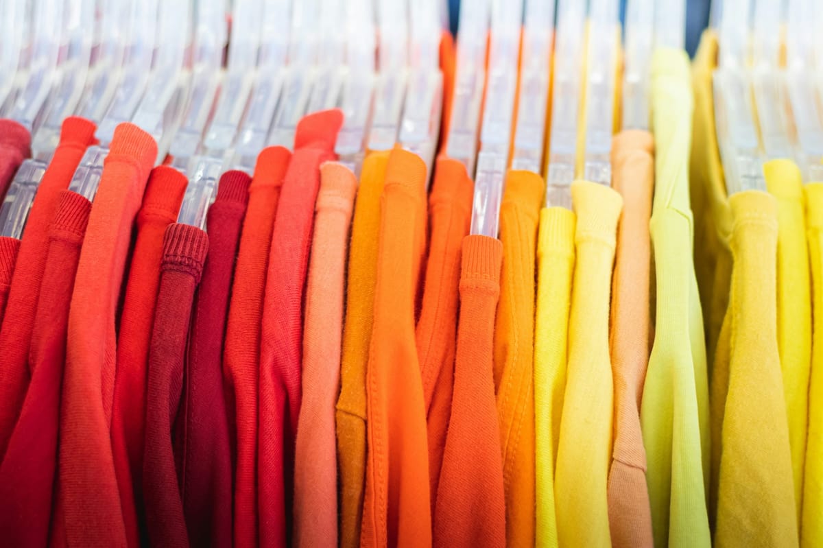Brightly colored shirts arranged in a gradient from red to yellow on hangers in a retail store.