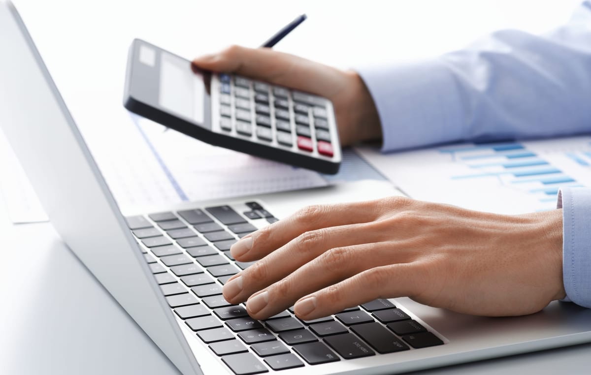 A person typing on laptop with a calculator in hand