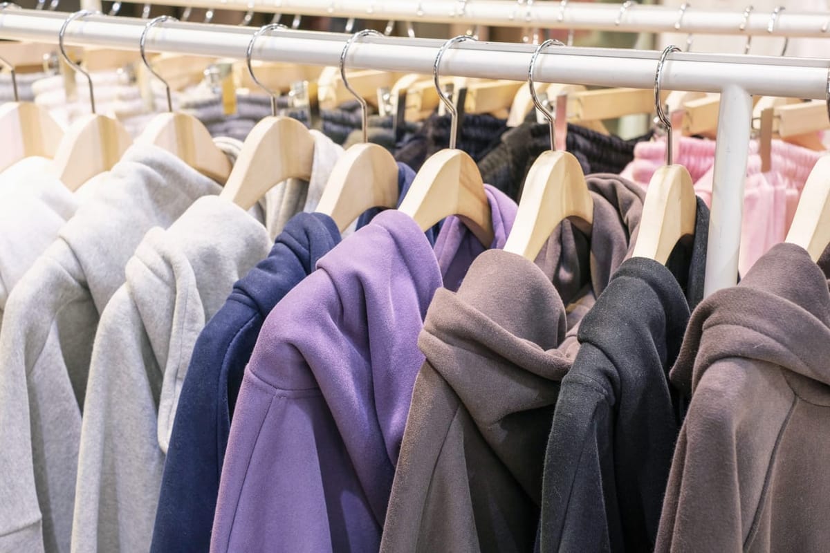 Row of hooded sweatshirts on wooden hangers on a clothing rack in assorted neutral and muted colors.