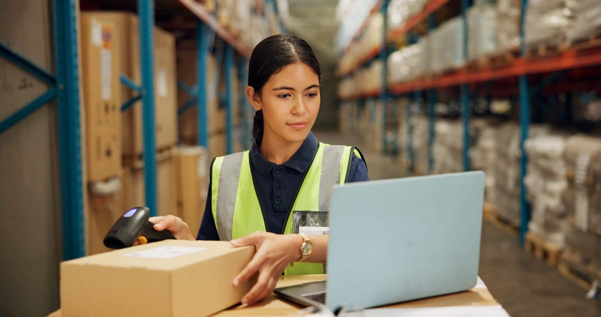 Female warehouse worker in a reflective vest using a barcode scanner while preparing a cardboard box for shipping.