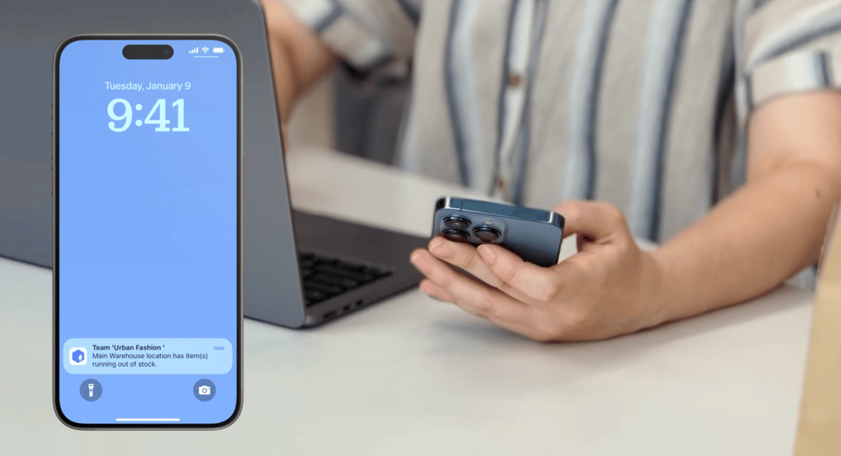 A person holding a smartphone with a BoxHero app push notification for low stock alert