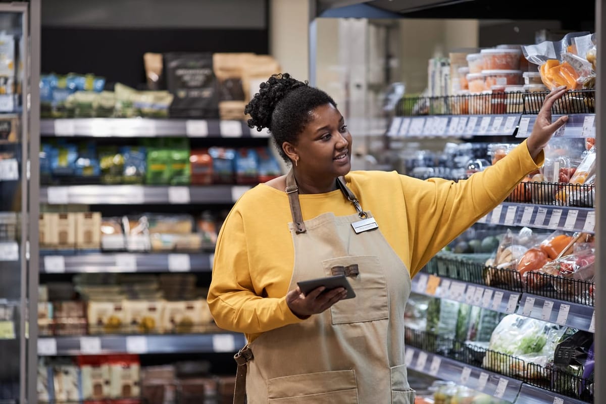 Waist up portrait of smiling black woman working in supermarket and wearing apron