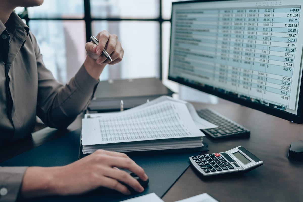 Office worker at the desk checking cost, balance, profit and currency data on monitor screen. Accounting and Financial concept.