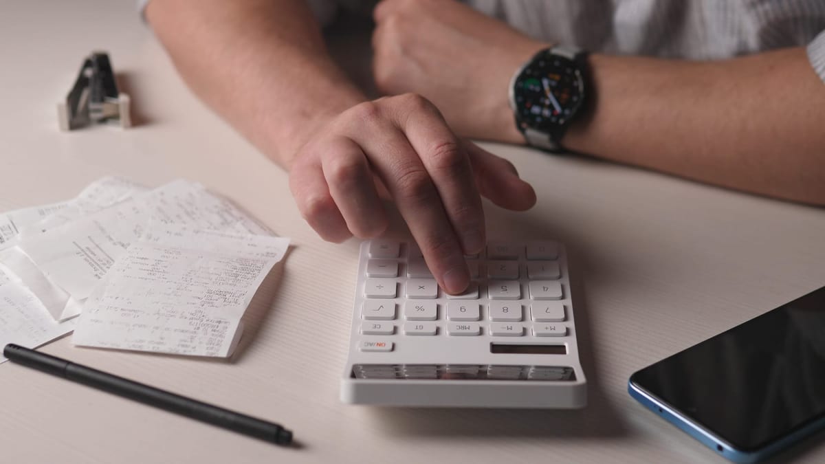 Wide-view hands reconciling a receipts/invoices with a calculator on a desk for financial records