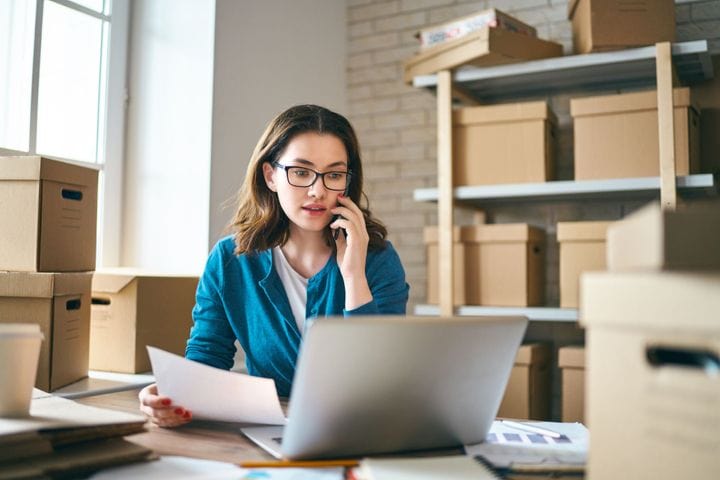 A woman calling a salesperson while looking at an invoice on her laptop.