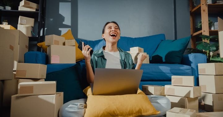 Young Asian female seller worker online store using mobile phone preparing parcel for shipment to client at home.