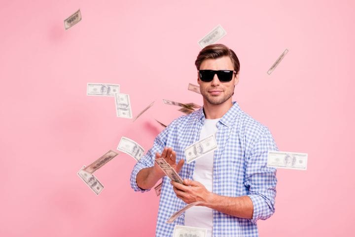 Portrait of a candid guy wearing checked shirt throwing money flying in air over pink pastel background